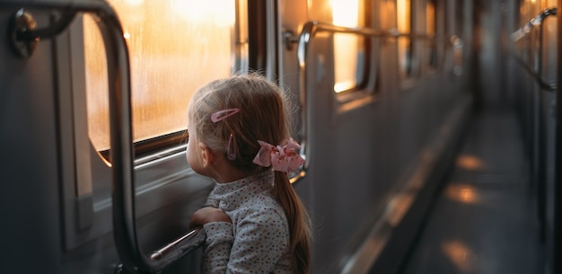 Bambina che guarda attraverso il finestrino del treno al tramonto