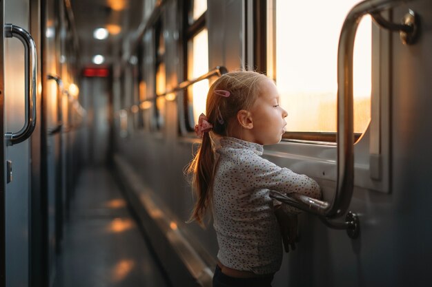 Bambina che guarda attraverso il finestrino del treno al tramonto