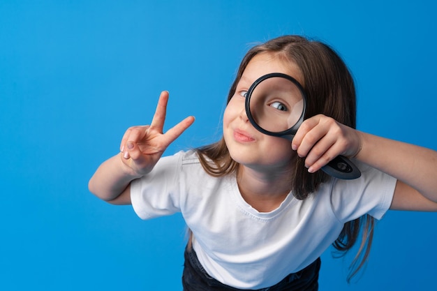 Bambina che guarda attraverso una lente d'ingrandimento su sfondo blu