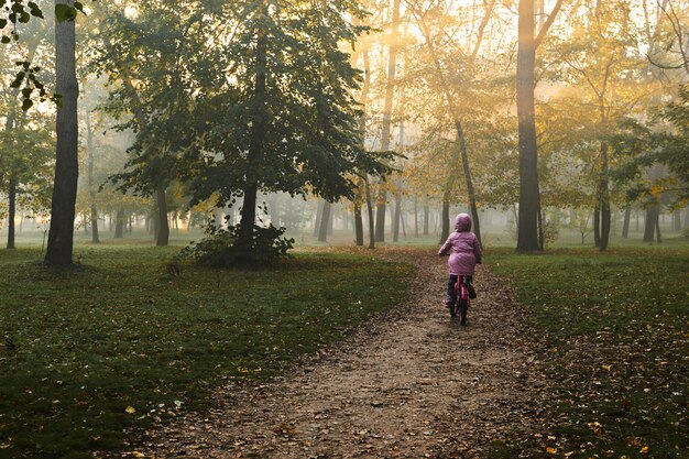 Bambina che guida la sua bici un bello giorno nebbioso di autunno all'alba