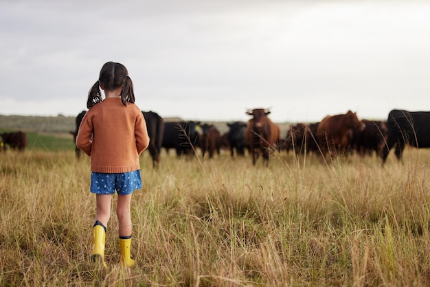 Bambina che impara l'agricoltura in una fattoria sostenibile con bovini ed esplora la natura all'aperto Vista posteriore di un bambino o un bambino spensierato che guarda le mucche o gli animali dei terreni agricoli che si godono la campagna