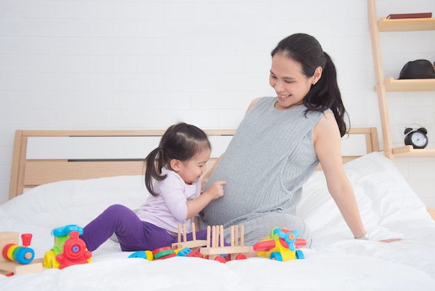 Bambina che indica la sua pancia della madre incinta e sorride