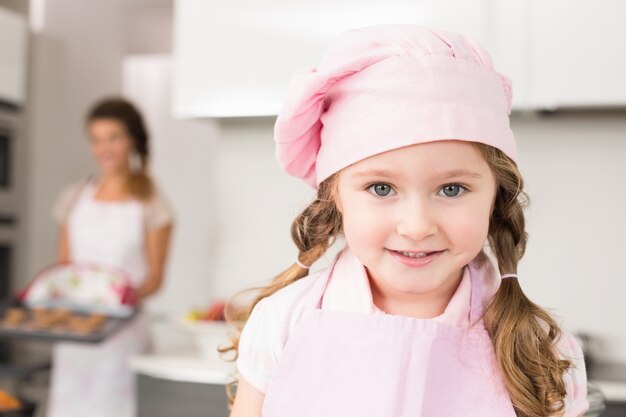 Bambina che indossa cappello rosa grembiule e chef a sorridere alla telecamera