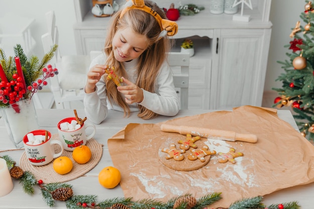 Bambina che indossa il cappello di Babbo Natale che cuoce i biscotti di Natale in cucina a casa.