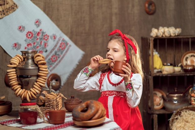 Bambina che indossa la fascia rossa e la camicia ornamentale bevendo tè dalla samovar che celebra Maslenitsa