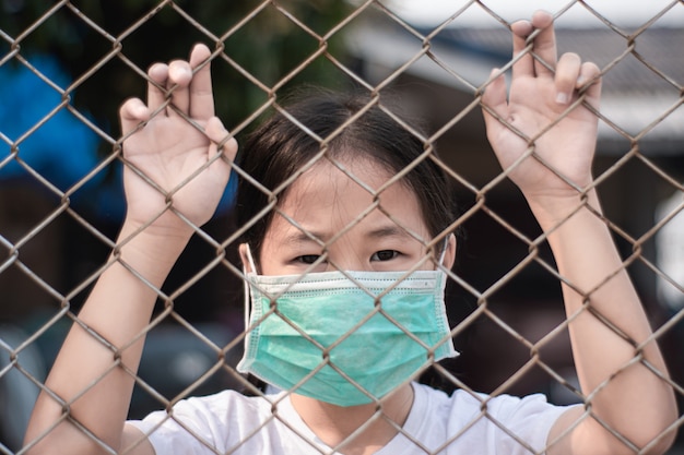 Bambina che indossa maschera protettiva medica in gabbia. Quarantena per protezione del coronavirus.