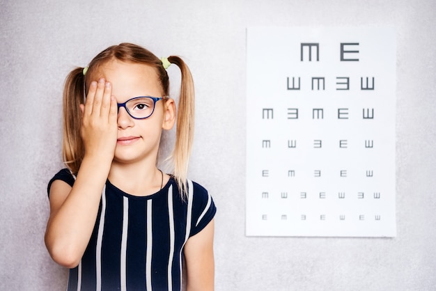 Bambina che indossa occhiali facendo il test della vista prima della scuola con un grafico sfocato sullo sfondo