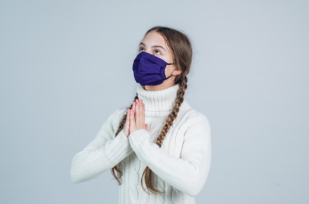 Bambina che indossa una maschera respiratoria per proteggersi dal coronavirus, prega.