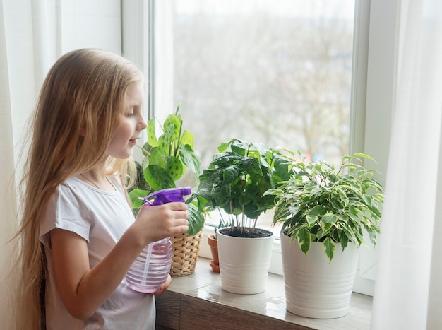 Bambina che innaffia le piante d'appartamento nella sua casa