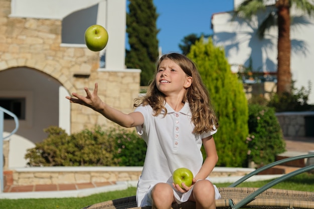 Bambina che lancia, gioca, giocoleria con le mele verdi