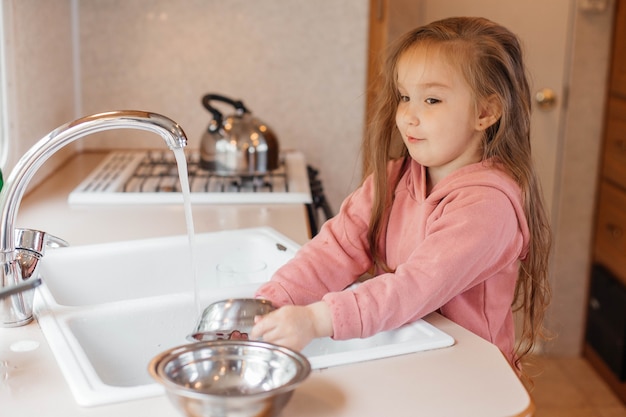 Bambina che lava i piatti nella cucina di una roulotte