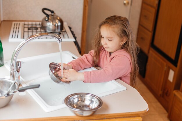 Bambina che lava i piatti nella cucina di una roulotte