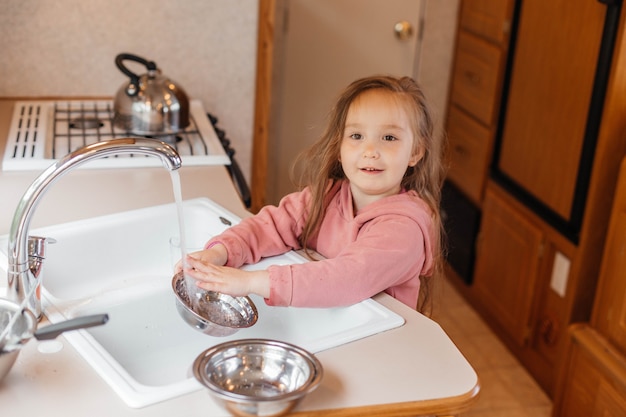 Bambina che lava i piatti nella cucina di una roulotte