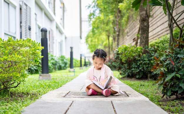 bambina che legge un libro con lo zaino che si siede nel parco pronto a tornare a scuola