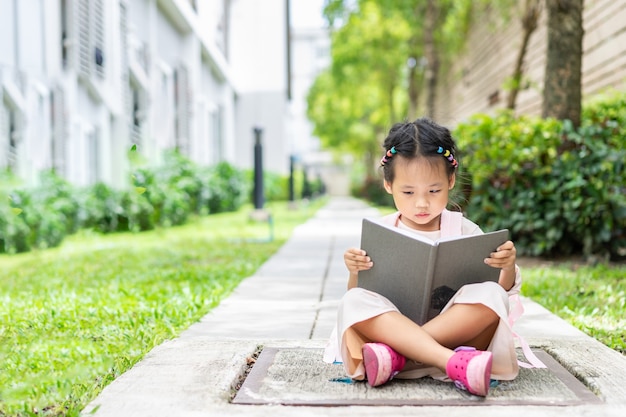 bambina che legge un libro con lo zaino che si siede nel parco pronto a tornare a scuola