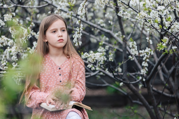 Bambina che legge un libro vicino ad un albero di fioritura