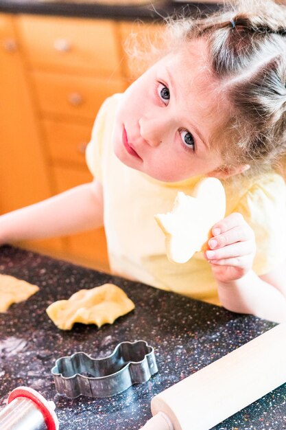 Bambina che mangia il biscotto di zucchero appena sfornato in cucina.