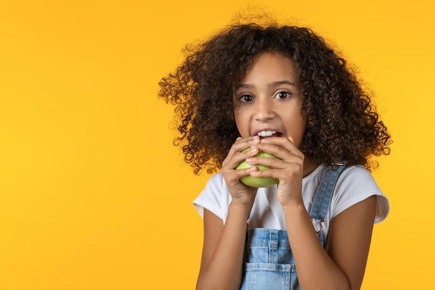 Bambina che mangia mela su sfondo giallo