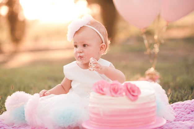 Bambina che mangia torta di compleanno cremosa con palloncini rosa