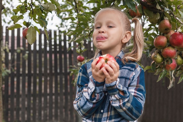 Bambina che mangia una mela in giardino vicino a melo