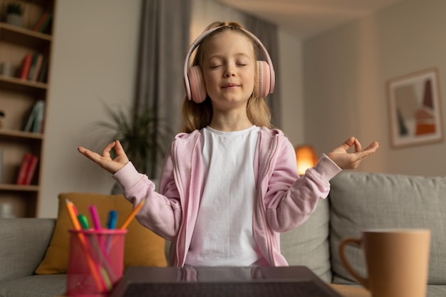 Bambina che medita online seduto vicino al computer portatile a casa