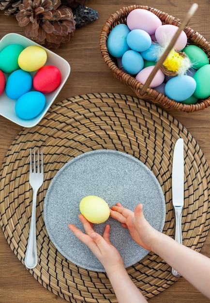 Bambina che mette l'uovo di Pasqua giallo su un piatto grigio durante la colazione di Pasqua