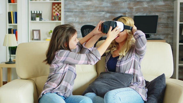 Bambina che mostra alla sua bella madre come usare le cuffie da realtà virtuale. Madre e figlia si divertono.