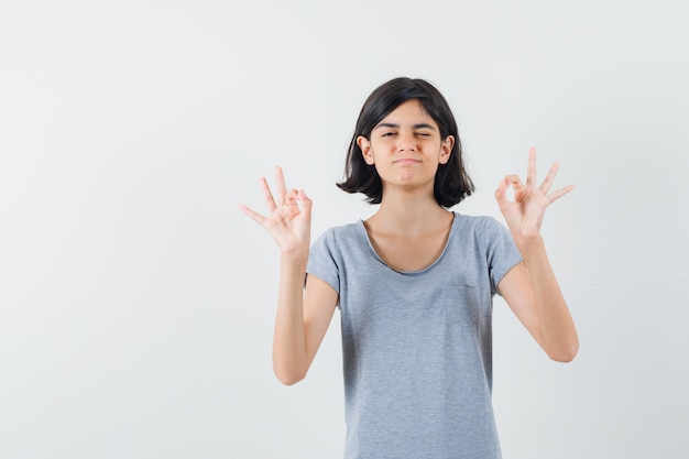 Bambina che mostra gesto di meditazione in maglietta e guardando fiducioso. vista frontale.