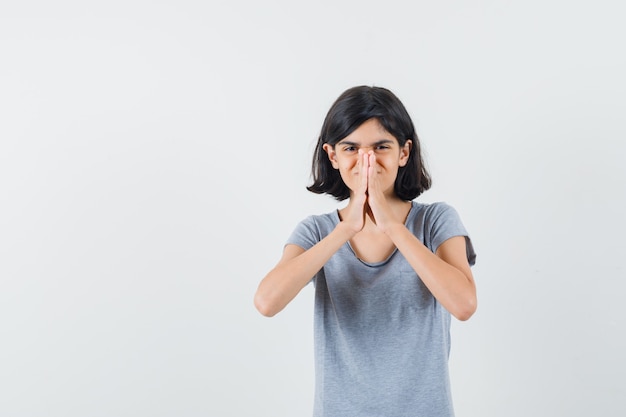 Bambina che mostra il gesto di namaste in maglietta e che sembra speranzoso, vista frontale.