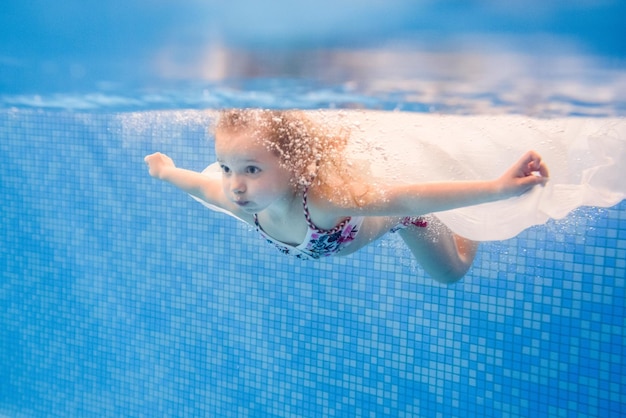 Bambina che nuota sott'acqua nella piscina per bambini Immersioni Imparare il bambino a nuotare Godetevi il nuoto e le bolle