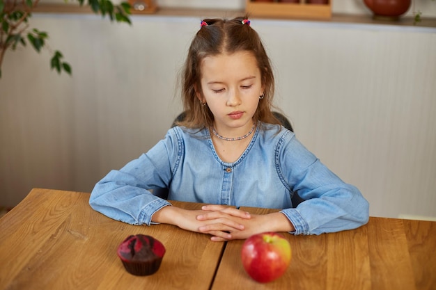 Bambina che osserva sulla torta dolce e sulla mela rossa fresca e scegliendo in cucina