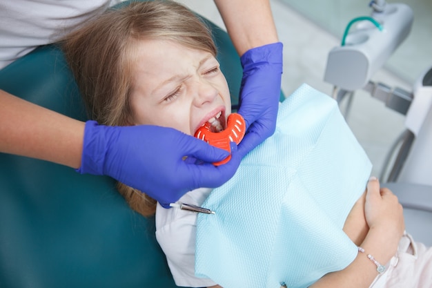 Bambina che piange sulla poltrona del dentista mentre il dentista fa impronte dentali con stucco