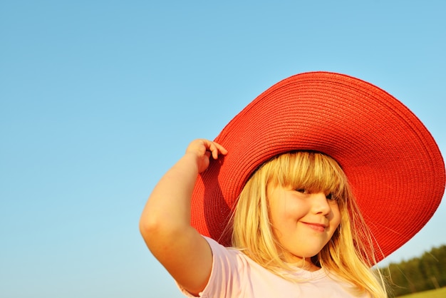 Bambina che porta cappello rosso sul prato di estate