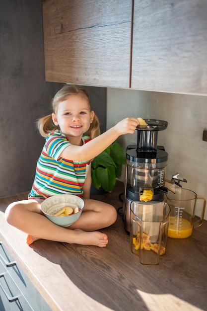 Bambina che produce succo fresco seduto sul tavolo nella cucina di casa