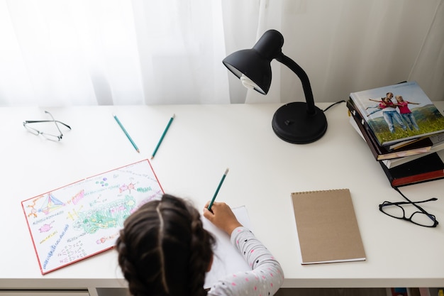 Bambina che ride, dipingendo matite colorate sul suo tavolo da gioco