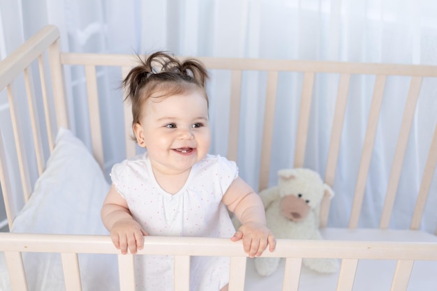 Bambina che ride felice nella culla nella scuola materna in un body bianco