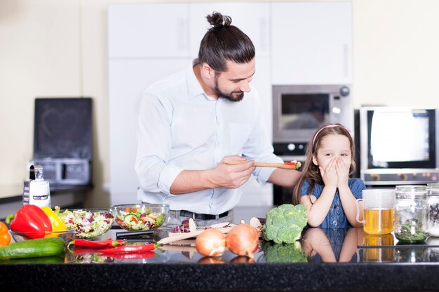 Bambina che rifiuta di mangiare insalata mentre cucina insieme al padre in cucina