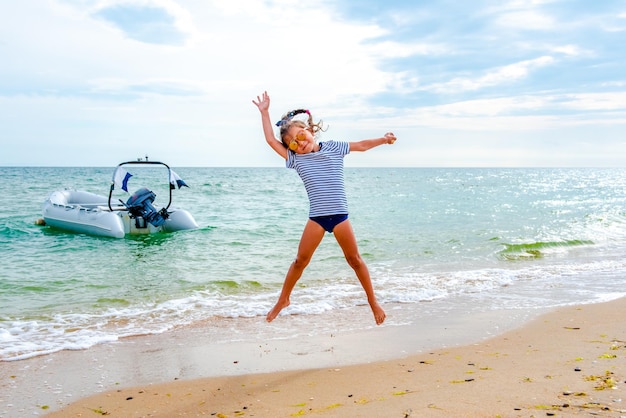 bambina che salta sulla spiaggia in riva al mare blu nelle vacanze estive durante il giorno