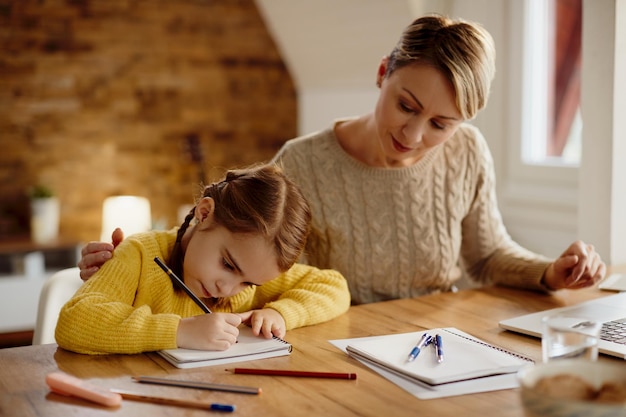 Bambina che scrive i compiti con l'aiuto di sua madre