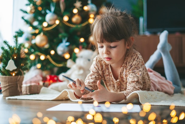 Bambina che scrive una lettera vicino all'albero di Natale