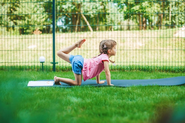 Bambina che si allunga sul tappetino a rullo praticando yoga all'aperto Yoga per bambini Uno stile di vita sano per bambini