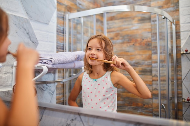 Bambina che si lava i denti con lo spazzolino da denti in legno ecologico in bagno