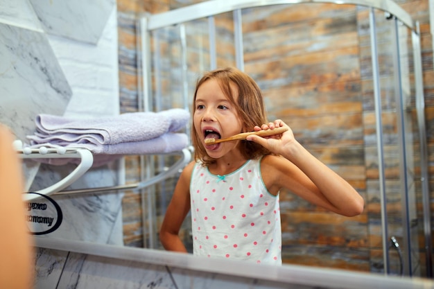 Bambina che si lava i denti con lo spazzolino da denti in legno ecologico in bagno