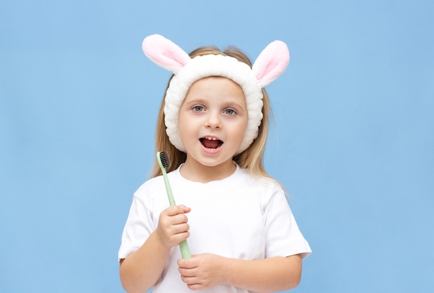 Bambina che si lava i denti e indossa le orecchie di coniglio su uno sfondo blu.