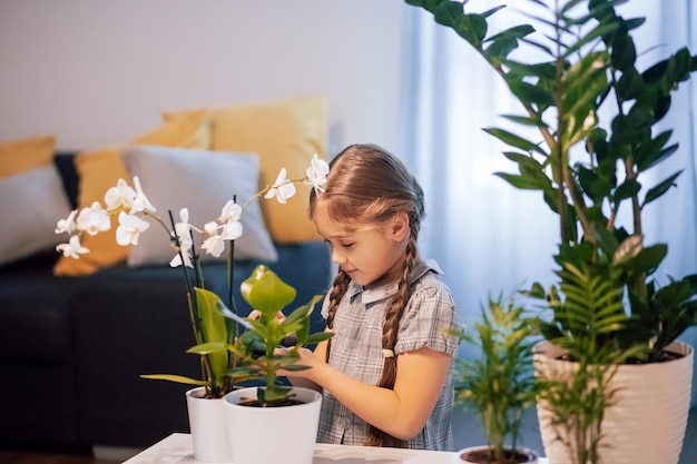 Bambina che si prende cura dei fiori in vaso. Le piante in casa. Fiori di casa. Ragazza che innaffia i fiori nella stanza