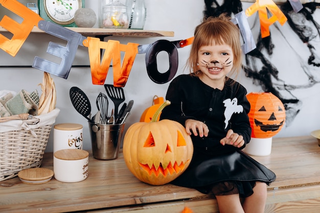 Bambina che si siede accanto alla zucca e che mostra un gesto spaventoso