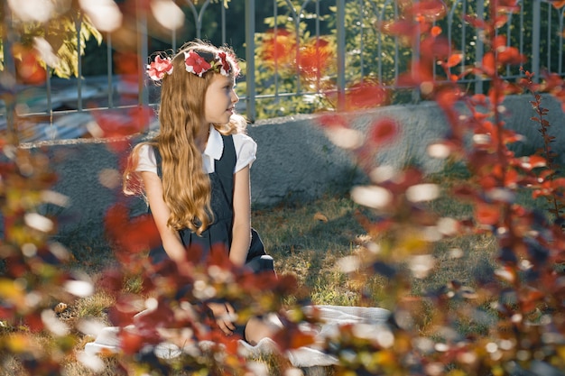 Bambina che si siede sul prato, ragazza bionda con lunghi capelli ondulati