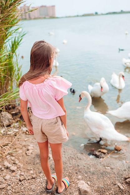 Bambina che si siede sulla spiaggia con i cigni