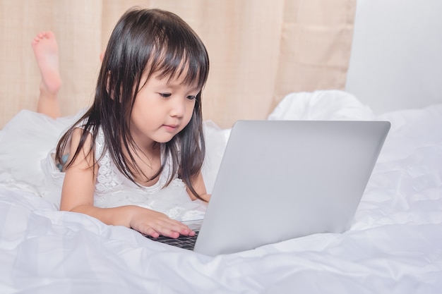 Bambina che si trova con il computer portatile sul sorridere felice del letto facendo uso di Internet con tecnologia