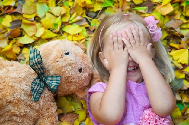 Bambina che si trova sulla strada sulle foglie cadute con la sua amica un orsacchiotto